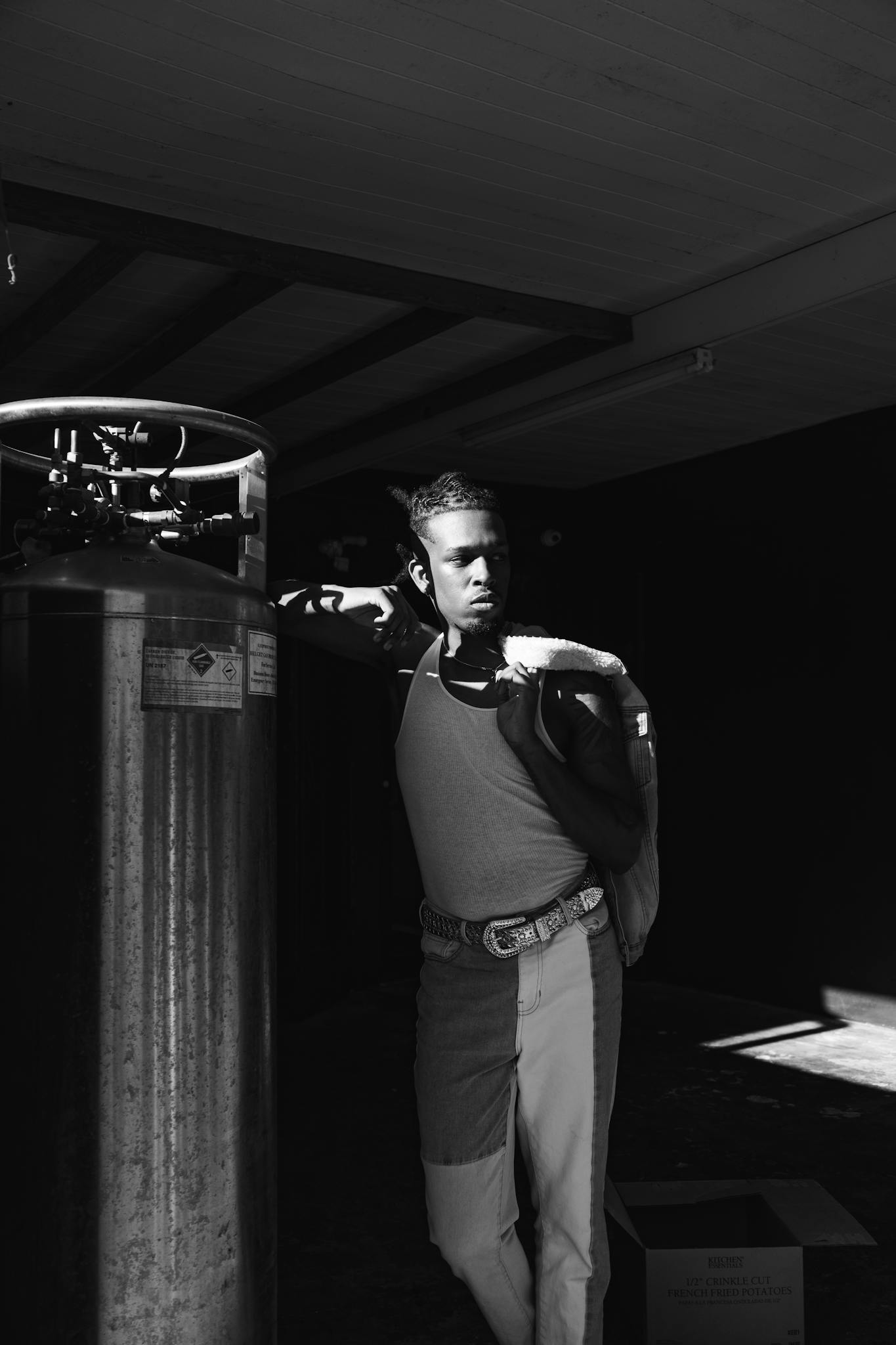 Black and white portrait of a stylish young man leaning on industrial equipment.